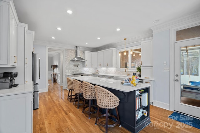 kitchen featuring a kitchen island, white cabinetry, light countertops, wall chimney exhaust hood, and decorative light fixtures