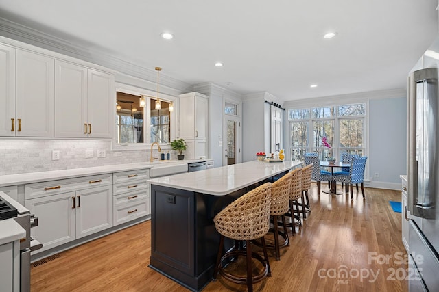 kitchen with a kitchen island, decorative light fixtures, stainless steel appliances, crown molding, and white cabinetry