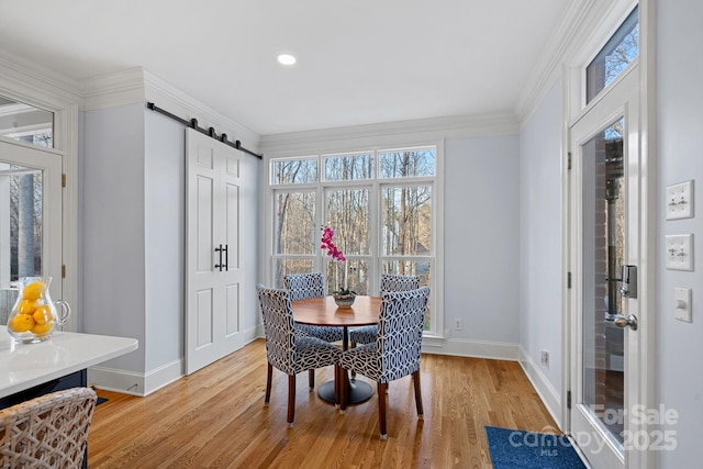 dining room with light wood-style floors, a barn door, baseboards, and crown molding