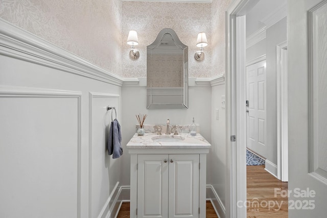 bathroom with wood finished floors, vanity, baseboards, and wallpapered walls