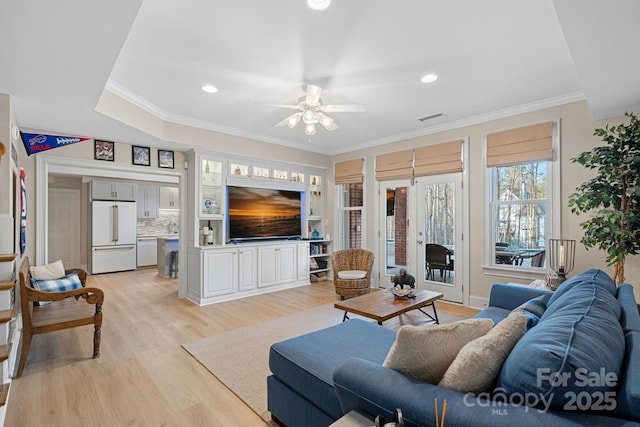 living room with light wood-type flooring, visible vents, a ceiling fan, and ornamental molding