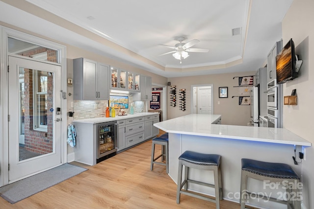 kitchen featuring light countertops, wine cooler, gray cabinets, and a kitchen bar