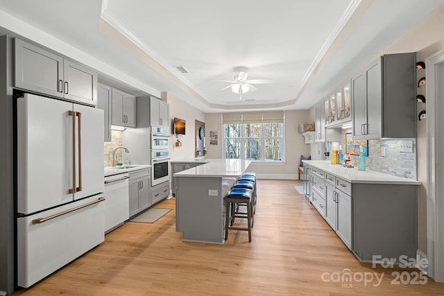 kitchen featuring a breakfast bar, white appliances, a raised ceiling, and light countertops