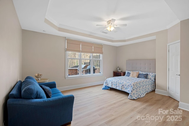 bedroom with light wood-style floors, a raised ceiling, crown molding, and baseboards