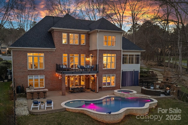 back of house at dusk featuring a balcony, brick siding, a pool with connected hot tub, an outdoor living space, and a patio area