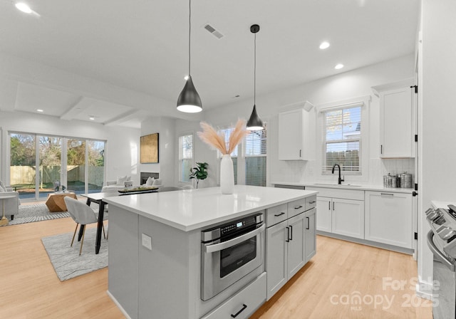 kitchen with white cabinetry, light wood-type flooring, a kitchen island, appliances with stainless steel finishes, and pendant lighting