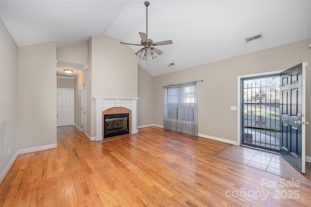 unfurnished living room with ceiling fan, a tile fireplace, high vaulted ceiling, and light wood-type flooring