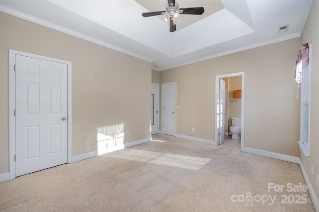 unfurnished bedroom with connected bathroom, crown molding, a tray ceiling, multiple windows, and light colored carpet