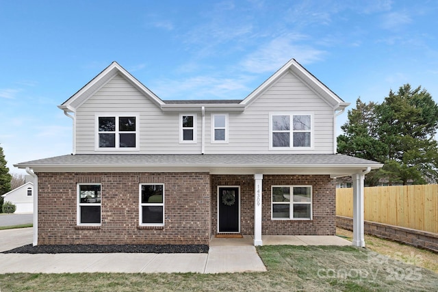 view of front of house with brick siding, a front yard, roof with shingles, and fence