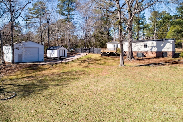 view of yard featuring an outbuilding, a storage unit, fence, a garage, and a wooden deck