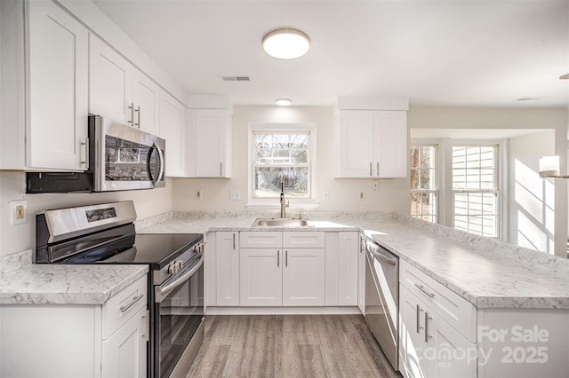 kitchen featuring sink, white cabinetry, light hardwood / wood-style flooring, kitchen peninsula, and stainless steel appliances