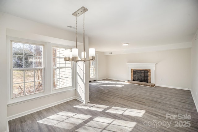 unfurnished living room featuring wood-type flooring, a brick fireplace, and a notable chandelier