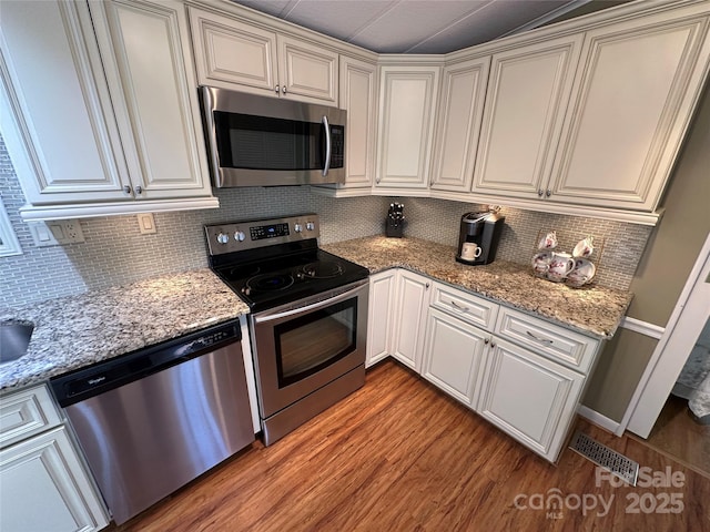 kitchen with stainless steel appliances, light stone counters, light wood-type flooring, and decorative backsplash