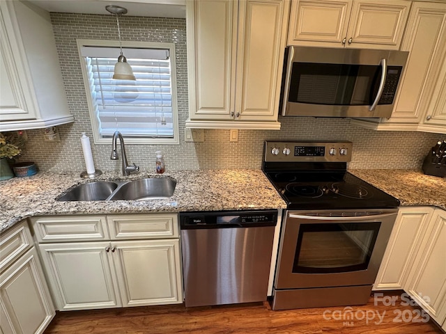 kitchen with appliances with stainless steel finishes, pendant lighting, sink, decorative backsplash, and light stone counters