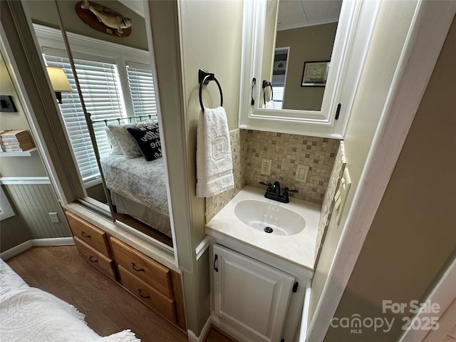 bathroom with hardwood / wood-style flooring, ornamental molding, vanity, and decorative backsplash