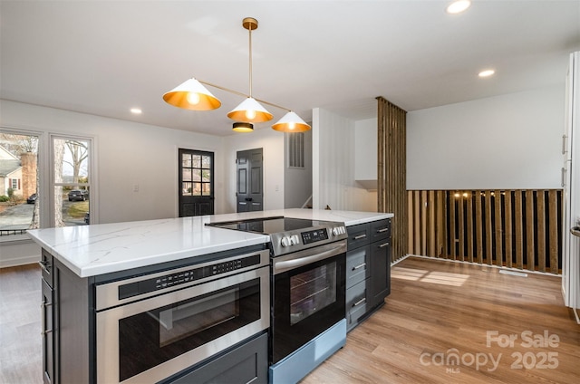 kitchen featuring stainless steel range with electric stovetop, hanging light fixtures, a center island, light stone countertops, and light wood-type flooring