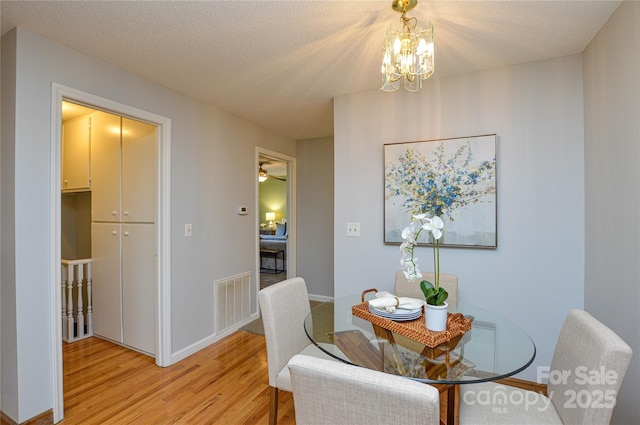 dining area with a notable chandelier, a textured ceiling, and light wood-type flooring