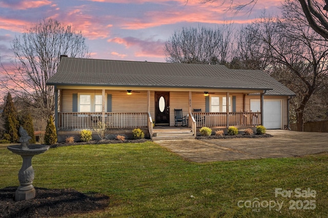 view of front facade with covered porch, a lawn, metal roof, a garage, and driveway