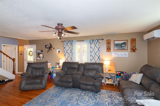 living room with hardwood / wood-style floors, a wall unit AC, a textured ceiling, and ceiling fan