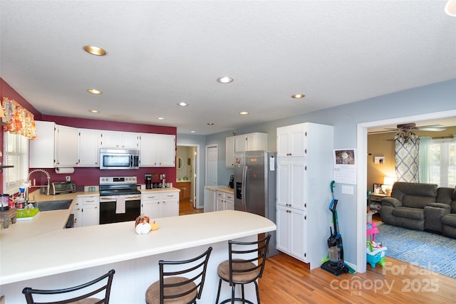 kitchen featuring light wood-type flooring, a kitchen breakfast bar, kitchen peninsula, stainless steel appliances, and white cabinets