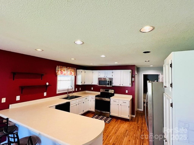 kitchen featuring light wood-style floors, a peninsula, white cabinets, appliances with stainless steel finishes, and a sink