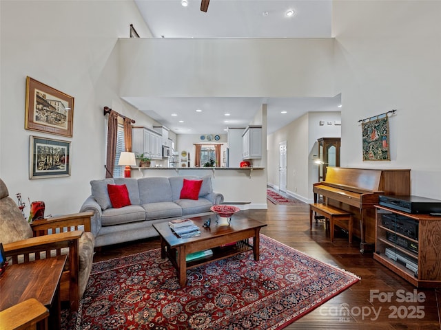 living room featuring dark hardwood / wood-style floors, ceiling fan, and a towering ceiling