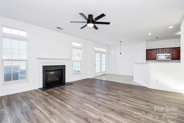 unfurnished living room with french doors, ceiling fan, light hardwood / wood-style floors, and a wealth of natural light