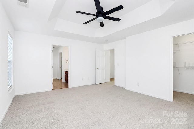 unfurnished bedroom featuring ensuite bathroom, a walk in closet, light colored carpet, a tray ceiling, and a closet