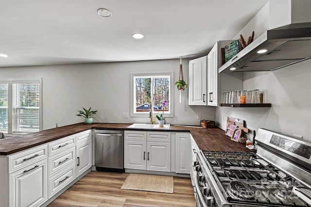 kitchen with wall chimney exhaust hood, white cabinetry, stainless steel appliances, and wooden counters