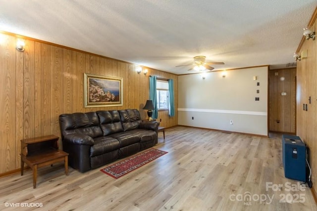 living room featuring wood walls, a textured ceiling, ceiling fan, and light hardwood / wood-style flooring