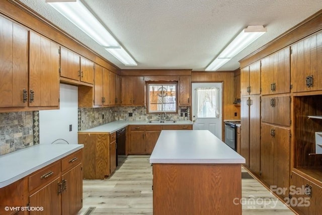 kitchen featuring dishwasher, sink, backsplash, a center island, and light wood-type flooring