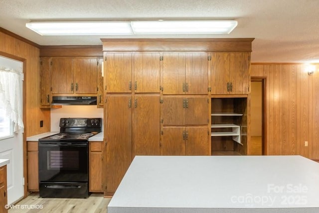 kitchen with crown molding, wooden walls, light wood-type flooring, and electric range