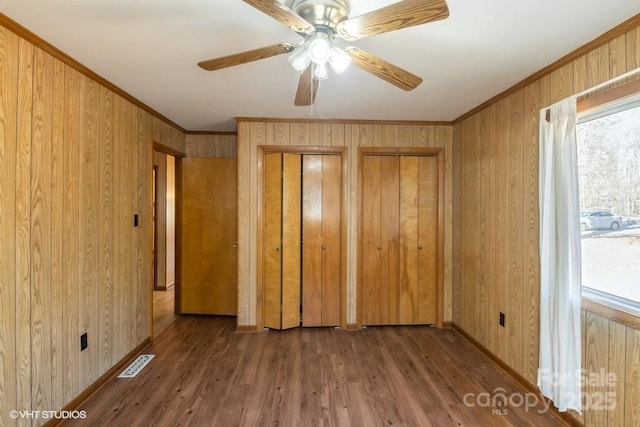 spare room featuring wood-type flooring, ornamental molding, wooden walls, and ceiling fan