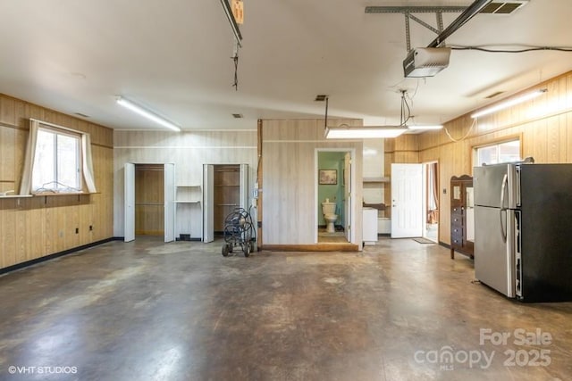 garage with a garage door opener, stainless steel refrigerator, and wood walls