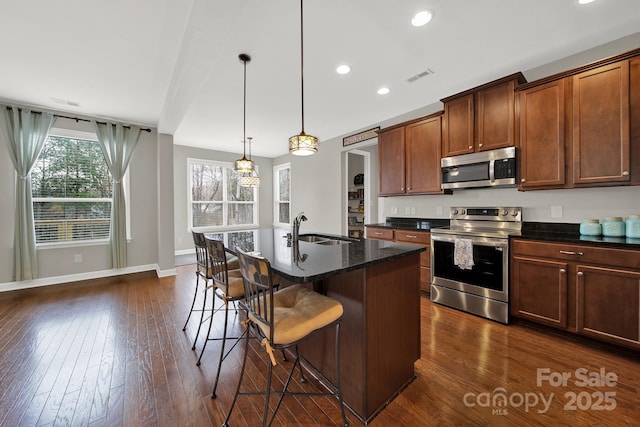 kitchen with dark wood-type flooring, sink, a breakfast bar area, an island with sink, and stainless steel appliances