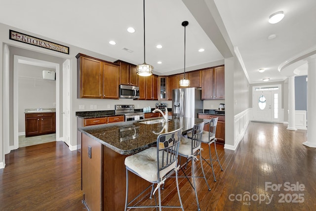 kitchen featuring decorative light fixtures, a center island with sink, a kitchen breakfast bar, stainless steel appliances, and decorative columns