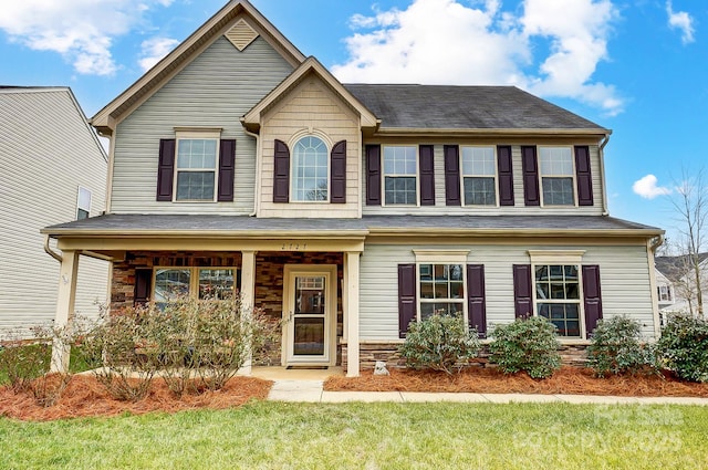 view of front of property with covered porch, stone siding, and a front yard