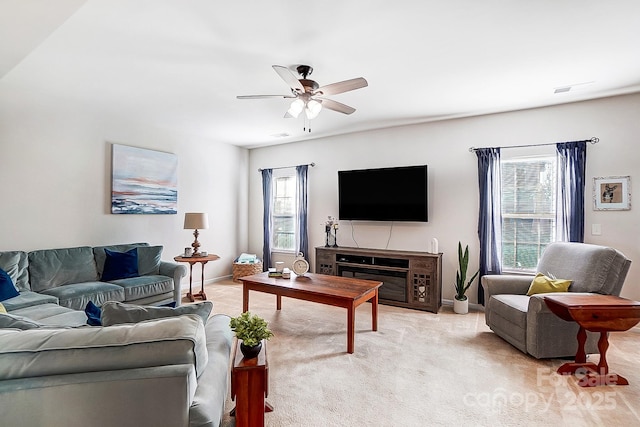 living room featuring a glass covered fireplace, light colored carpet, ceiling fan, and baseboards