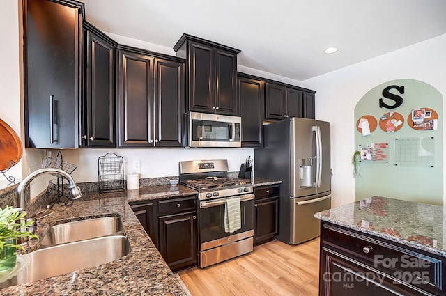 kitchen featuring light wood finished floors, dark stone countertops, stainless steel appliances, a sink, and recessed lighting