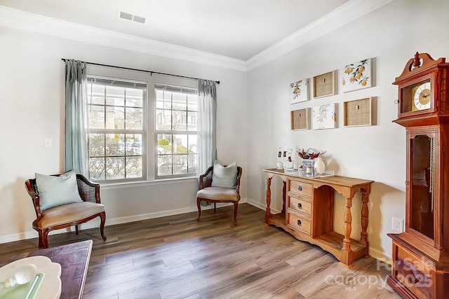 sitting room with light wood finished floors, baseboards, visible vents, and crown molding