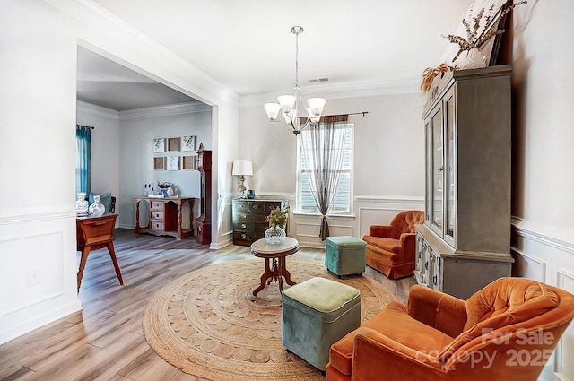 sitting room with light wood finished floors, a chandelier, crown molding, and a wainscoted wall