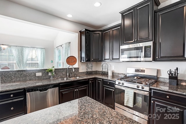 kitchen with recessed lighting, dark cabinets, a sink, appliances with stainless steel finishes, and dark stone counters