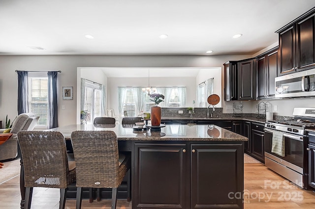 kitchen with dark stone counters, a kitchen island, a breakfast bar, stainless steel appliances, and a sink