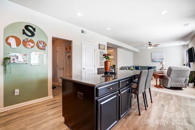 kitchen with light wood finished floors, visible vents, dark stone counters, and a center island