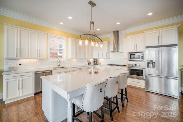 kitchen featuring appliances with stainless steel finishes, pendant lighting, sink, a center island, and wall chimney exhaust hood