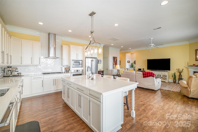 kitchen featuring a breakfast bar area, decorative light fixtures, a center island with sink, stainless steel appliances, and wall chimney range hood