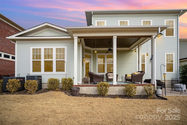 back house at dusk featuring central AC unit, a lawn, a patio, and ceiling fan