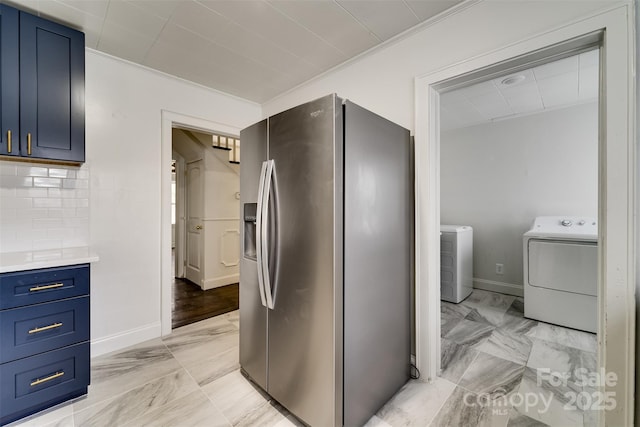 kitchen featuring washer and clothes dryer, blue cabinetry, tasteful backsplash, ornamental molding, and stainless steel fridge with ice dispenser