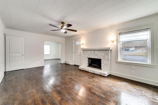 unfurnished living room featuring dark wood-type flooring, ceiling fan, a stone fireplace, and crown molding