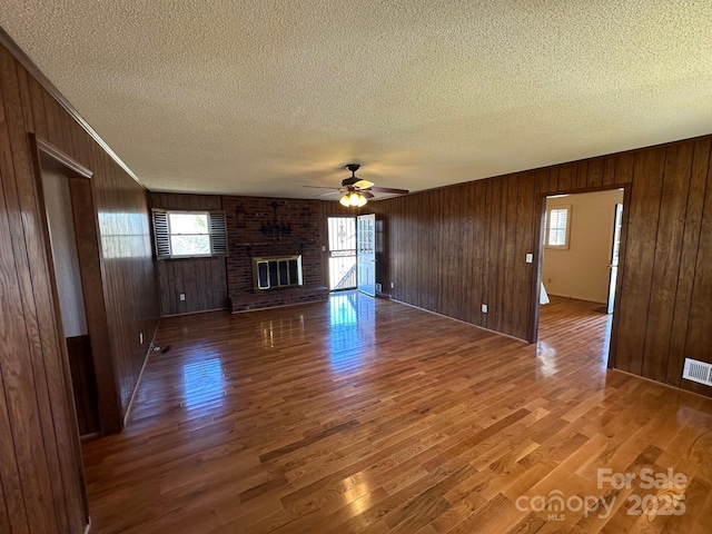 unfurnished living room with hardwood / wood-style floors, a fireplace, wood walls, ceiling fan, and a textured ceiling